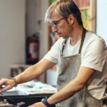 store-owner-wearing-eyeglasses-using-cash-register-at-checkout-in-organic-market-model-released-symb.webp
