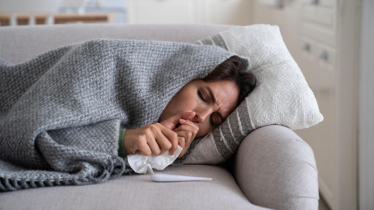 Young-woman-lying-under-blanket-on-sofa-coughing-and-sneezing-using-paper-tissue-to-blow-her-nose-Un.jpeg