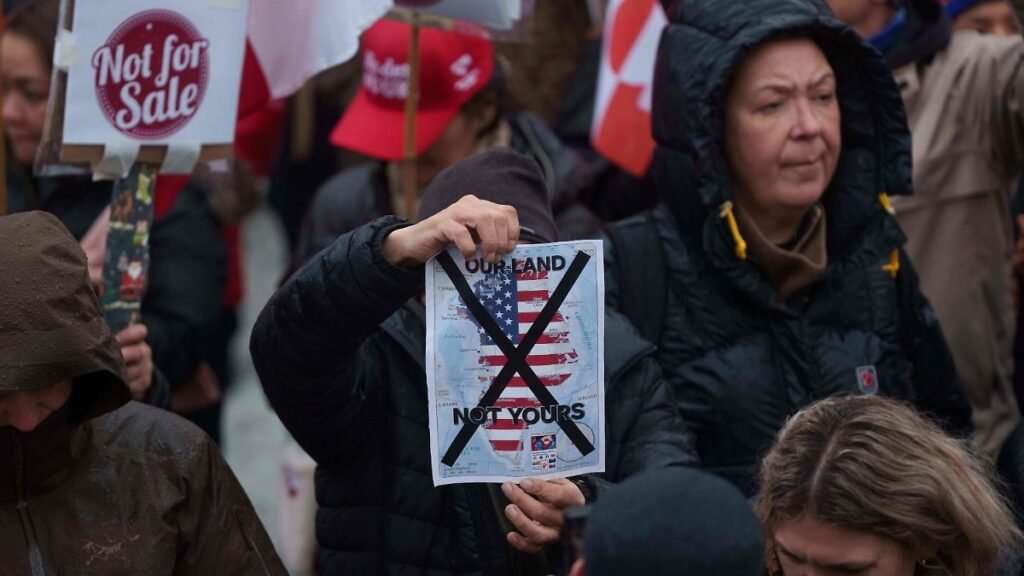 A-man-holds-a-map-of-Greenland-covered-in-the-American-flag-crossed-out-with-an-X-during-a-protest-a.jpeg
