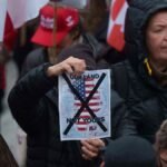 A-man-holds-a-map-of-Greenland-covered-in-the-American-flag-crossed-out-with-an-X-during-a-protest-a.jpeg