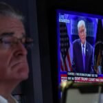 A-trader-works-on-the-floor-as-a-screen-displays-U-S-President-Donald-Trump-during-a-press-briefing.jpeg