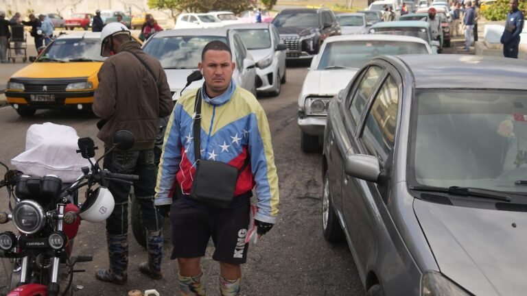Ein-Mann-der-eine-Jacke-in-den-Farben-der-venezolanischen-Flagge-traegt-steht-an-einer-Tankstelle-an.jpeg