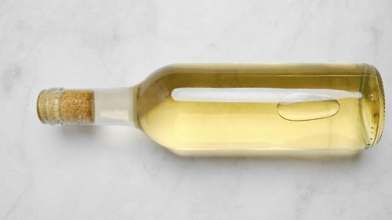Eine-Glasflasche-mit-Weisswein-auf-einer-glatten-hellen-Oberflaeche-Die-Flasche-hat-einen-Korkdeckel.jpeg