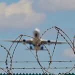 Symbolbild-Abschiebeflug-Ein-startendes-Flugzeug-hinter-einem-Stacheldrahtzaun.jpg