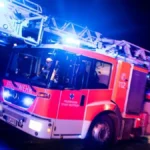 ein-drehleiterwagen-der-feuerwehr-faehrt-mit-blaulicht-an-einer-unfallstelle-vorbei-symbolbild-in-du.webp