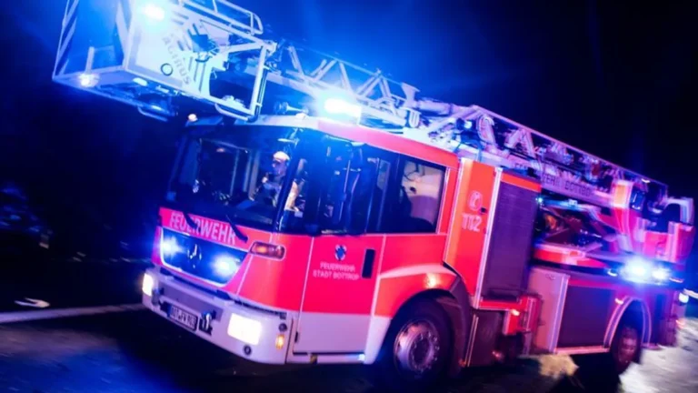 ein-drehleiterwagen-der-feuerwehr-faehrt-mit-blaulicht-an-einer-unfallstelle-vorbei-symbolbild-in-du.webp