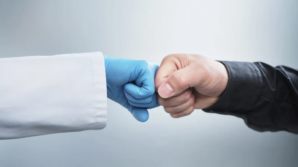 female-healthcare-worker-giving-fist-bump-to-male-patient-against-white-background.webp