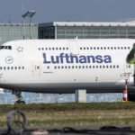 Ein-Bauarbeiten-steht-auf-der-Start-und-Landebahn-waehrend-eine-Lufthansa-Maschine-im-Hintergrund-fa.jpeg