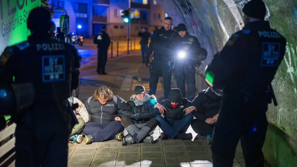 mehrere-gegendemonstranten-sitzen-im-tafelfeldtunnel-in-nuernberg-auf-der-fahrbahn-und-bilden-eine-s.webp