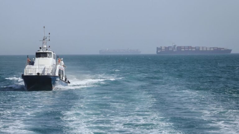 02-05-2026-Iran-Bandar-Abbas-Ein-Patrouillenboot-faehrt-durch-das-Wasser-waehrend-Frachtschiffe-in-d.jpeg