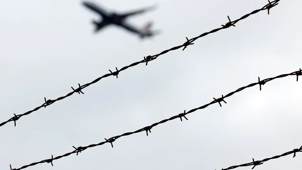 ein-flugzeug-startet-am-flughafen-koeln-bonn-gesehen-durch-stacheldraht-ausserhalb-des-rollfelds-der.webp
