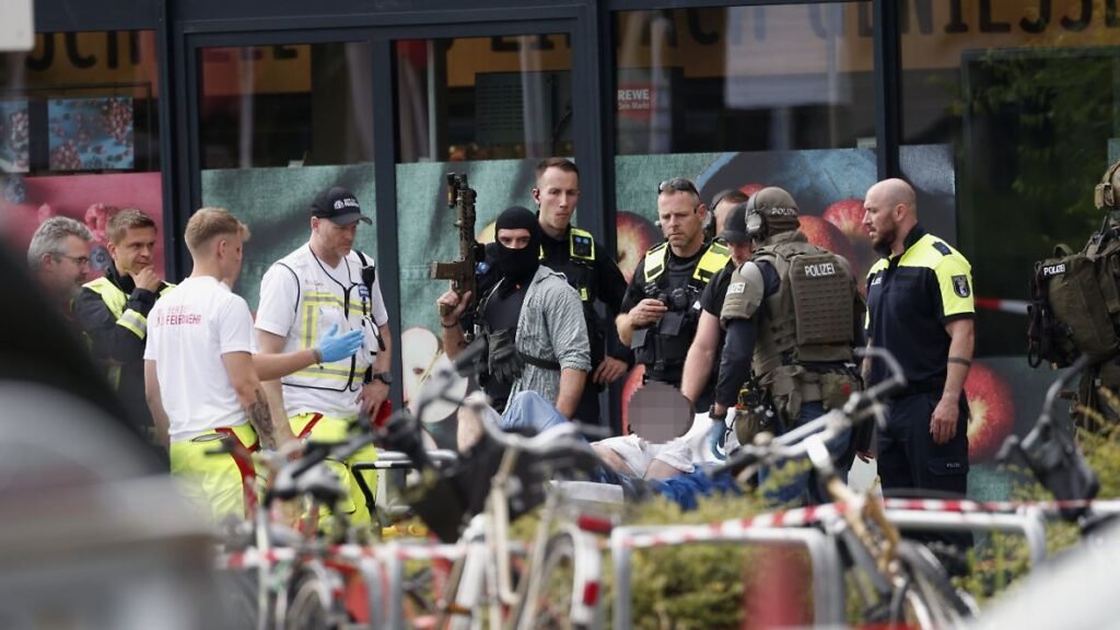 Einsatzkraefte-stehen-vor-einem-Supermarkt-neben-einer-verletzten-Person-auf-einer-Trage-In-dem-Supe.jpeg