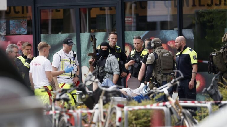 Einsatzkraefte-stehen-vor-einem-Supermarkt-neben-einer-verletzten-Person-auf-einer-Trage-In-dem-Supe.jpeg