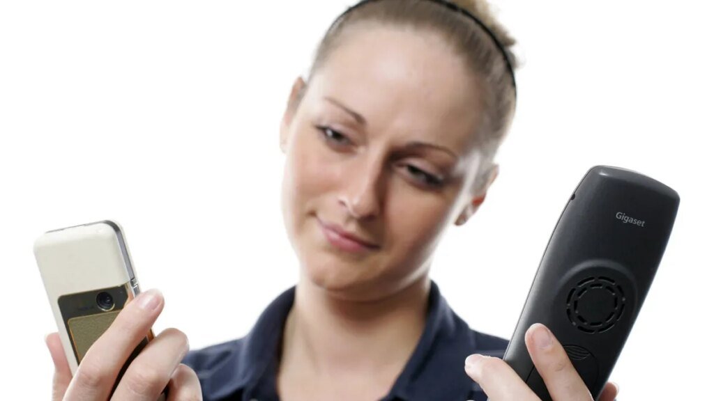 junge-frau-muss-sich-zwischen-ihrem-handy-oder-einem-festnetztelefon-entscheiden.jpg